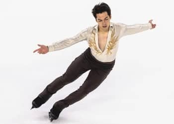 Wearing a white top and black pants, with arms extended, Camden Pulkinen glides across the ice at Grand Prix de France